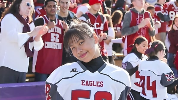 Una joven con una camiseta blanca de Eagles se encuentra frente a un grupo de personas con camisetas rojas en el campus de la Layton Christian Academy.