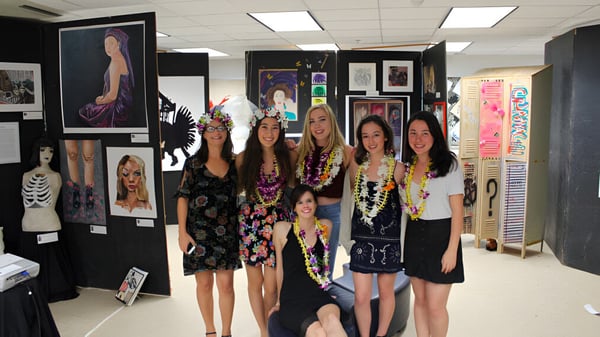 Un grupo de jóvenes estudiantes de la Le Jardin Academy está junto en una exposición de arte con varias obras de arte enmarcadas.