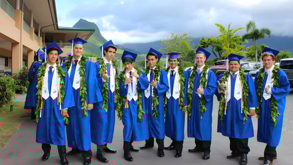 Un grupo de graduados de la Le Jardin Academy está al aire libre frente a un paisaje tropical.
