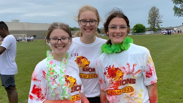 Tres alumnas de la Leamington District Secondary School posan sonriendo al aire libre en un campo.