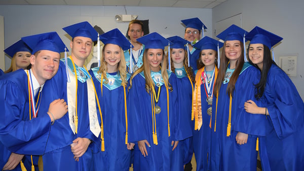 Un grupo de graduados en togas azules celebra su graduación en un aula de Lee Academy.