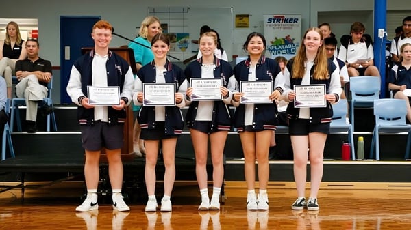 Un grupo de jóvenes alumnas de la Leeming Senior High School sostiene certificados en un gimnasio.