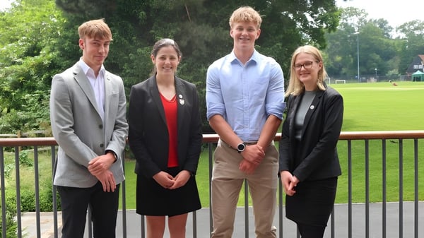 Cuatro estudiantes de la Leighton Park School están en un balcón con vista a un parque cubierto de hierba.