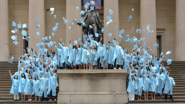 Estudiantes de la Léman Manhattan Preparatory School se reúnen en túnicas azules alrededor de una gran estatua en una escalera.