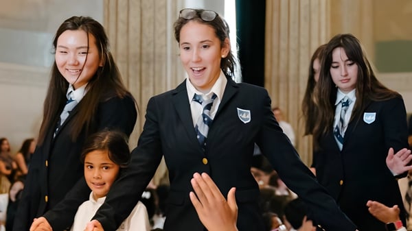 Un grupo de estudiantes en uniformes escolares está junto a la Léman Manhattan Preparatory School en un entorno formal.