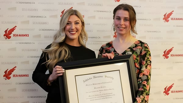 Dos alumnas de la Leo Burke Academy sostienen un certificado enmarcado frente a un logo de Seahawks.