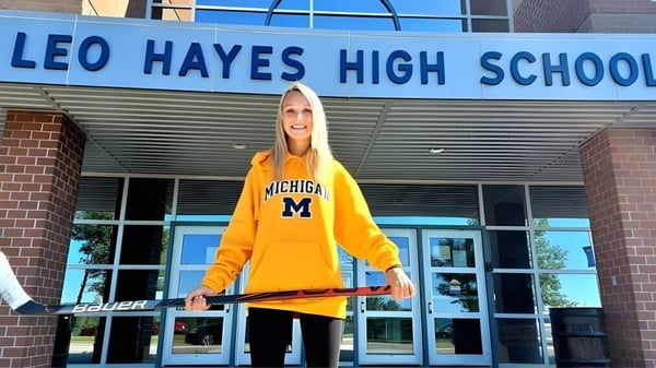 Una estudiante con sudadera amarilla de Michigan está frente a la entrada de la Leo Hayes High School.