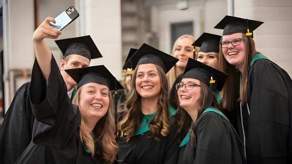 Un grupo de graduadas y graduados del Lethbridge Collegiate Institute posan con vestimenta de graduación frente a un edificio universitario.