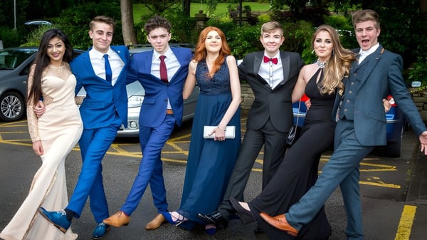 Un grupo de personas bien vestidas en el campus de la Lewes Old Grammar School frente a un fondo verde.