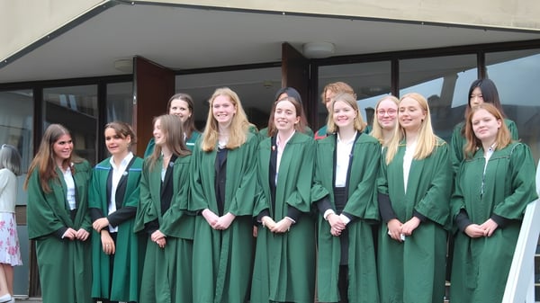 Un grupo de jóvenes alumnas de Leweston School está en túnicas de graduación verdes frente a un edificio con un pasillo cubierto.