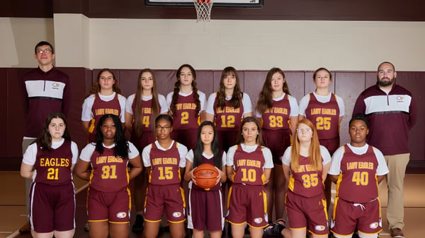 Un grupo de estudiantes de la Liberty Christian Academy posan en camisetas de baloncesto en el gimnasio frente al aro de baloncesto.