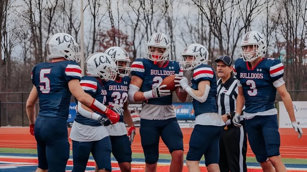 Un grupo de futbolistas está en el campo de la Liberty Christian Academy frente a un fondo boscoso.