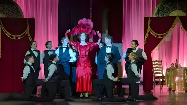 Estudiantes de la Liberty Christian Academy están vestidos formalmente y con un disfraz rojo en un escenario con cortinas decorativas.