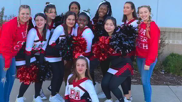 Un grupo de animadoras con uniformes rojos y blancos está frente a una pared azul en el campus de la Life Prep Academy.