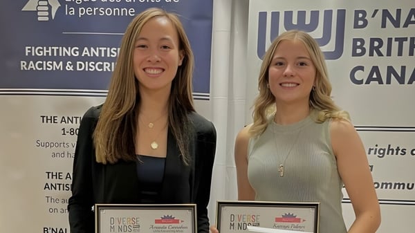 Dos mujeres sonriendo están frente a pancartas de la organización anti-racismo en el terreno de la Lillian Osborne High School.