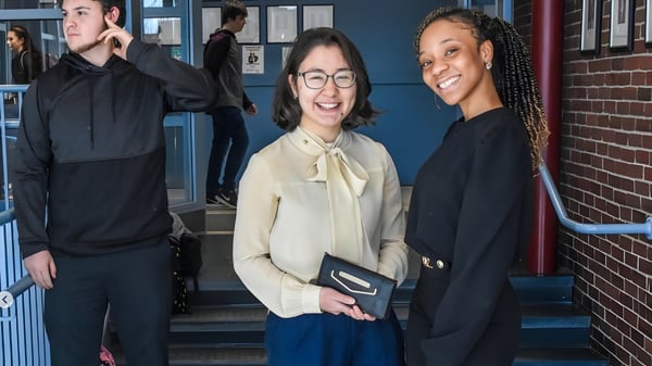 Tres personas están de pie en una escalera frente a un edificio de ladrillo en el campus de la Lincoln Academy.