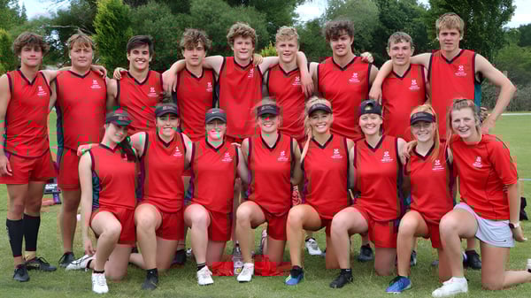 Un grupo de estudiantes de la Lincoln High School en uniformes deportivos rojos posan juntos al aire libre frente a un paisaje verde.