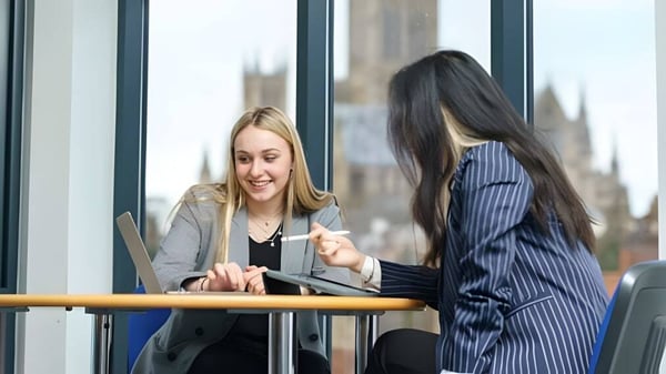 Dos mujeres están frente a una ventana con vista a la ciudad en el campus de la Lincoln Minster School y mantienen una conversación.