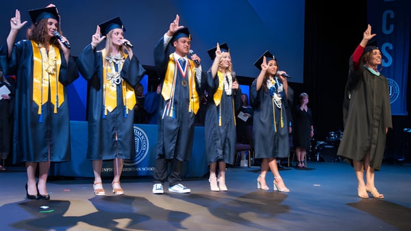 Los graduados de la Linfield Christian School están en un escenario celebrando su graduación con togas amarillas y negras.