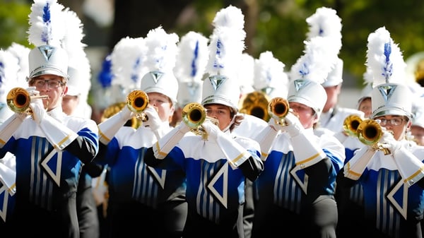 La banda marcial del Lisgar Collegiate Institute toca al aire libre frente a un fondo verde.