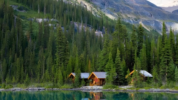 Un tranquilo paisaje montañoso con un lago y cabañas, rodeado de bosques, sin relación directa con el Lisgar Collegiate Institute.
