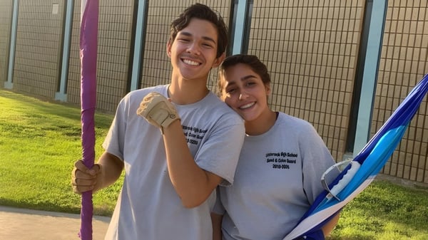 Dos personas sonrientes están en el campus de la Littlerock High School frente a un área de césped y una cerca.