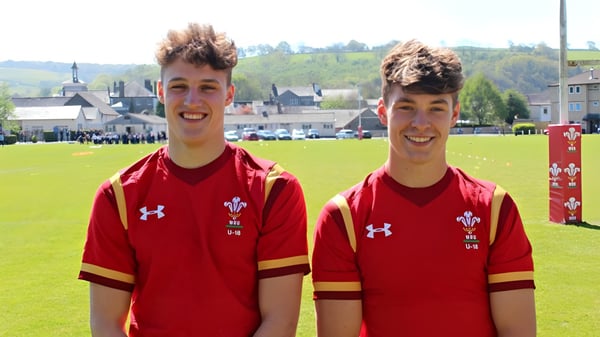Dos estudiantes del Llandovery College están en un campo de césped con camisetas deportivas rojas y el escudo de Gales.