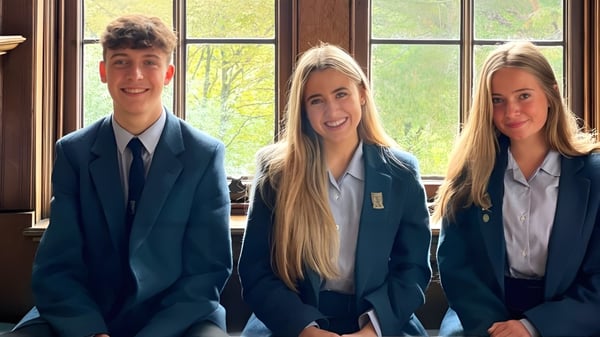 Tres alumnos de la Lomond School están de pie frente a una gran ventana con vista a árboles y áreas verdes.