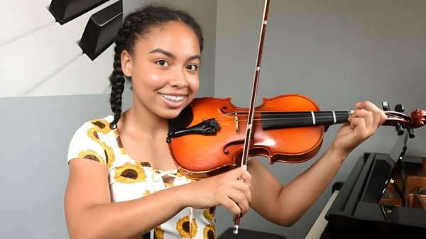 Una estudiante de la London Central Secondary School toca el violín en una sala con instrumentos musicales de fondo.
