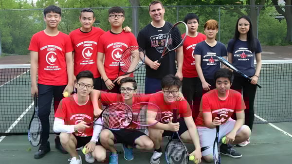 Un grupo de estudiantes de la London International Academy posan juntos en una cancha de tenis con camisetas rojas.