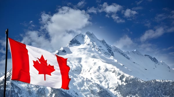 Un pico montañoso cubierto de nieve con una bandera canadiense ondeando frente a un cielo despejado en el terreno del London South Collegiate Institute.