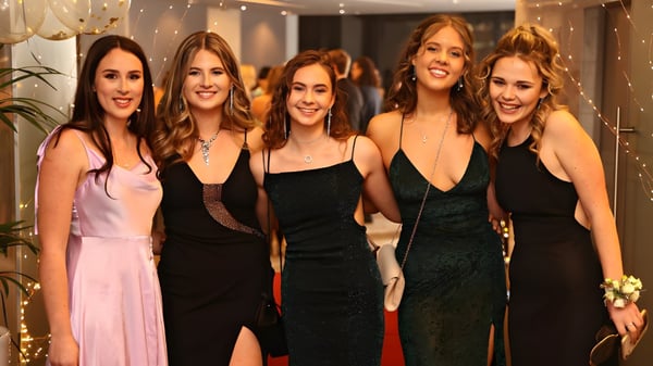 Cinco alumnas del Long Bay College posan juntas en una habitación débilmente iluminada con luces de cadena de fondo.
