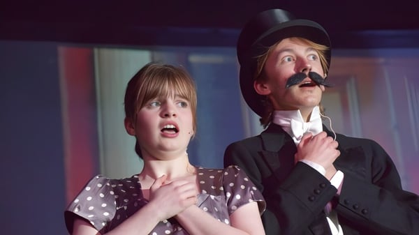 Una mujer con expresión sorprendida y un hombre con bigote están en una sala débilmente iluminada de la Longridge Towers School.