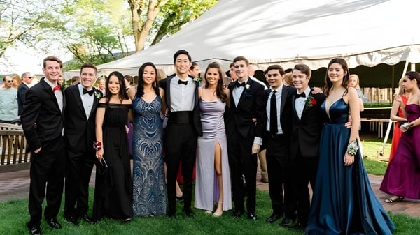 Un grupo de estudiantes de la Loomis Chaffee School en ropa formal posan al aire libre frente a una carpa y árboles.