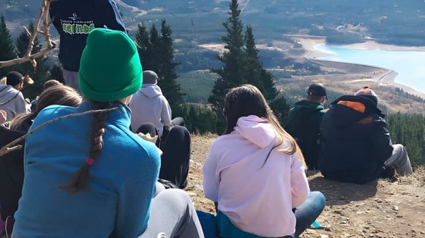 Un grupo de estudiantes de la Lord Beaverbrook High School está en una colina mirando un paisaje montañoso con una carretera.