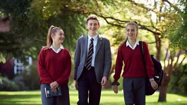 Tres estudiantes del Lord Wandsworth College caminan juntos por un camino cubierto de hierba entre árboles en el campus.