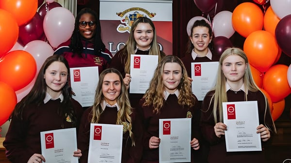 Un grupo de jóvenes graduadas del Loreto College Cavan posan con diplomas frente a globos y el logo de la escuela.