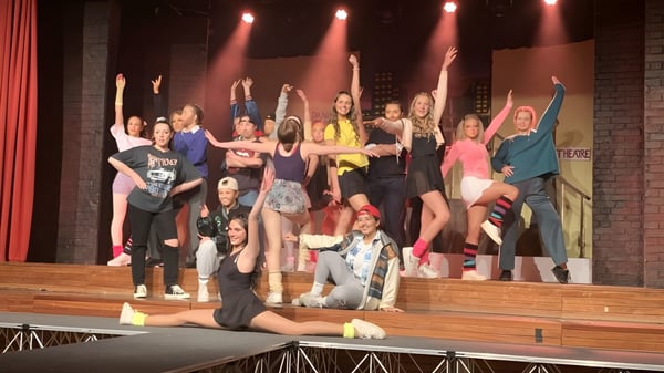 Alumnas y alumnos de la Loreto High School Beaufort están en el escenario durante una actuación con iluminación colorida.