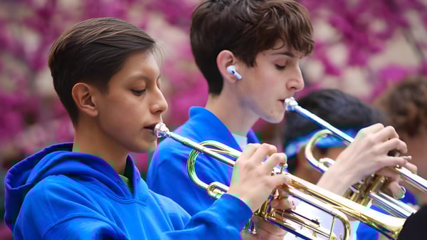 Dos estudiantes del Los Angeles Unified School District tocan instrumentos de metal frente a flores violetas.