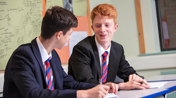 Dos estudiantes de la Loughborough Grammar School conversan en una mesa de aula frente a una pizarra.