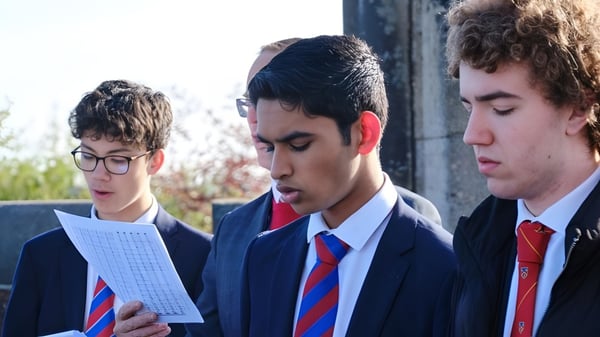 Tres estudiantes de la Loughborough Grammar School discuten junto con una hoja de papel al aire libre frente a un edificio escolar.