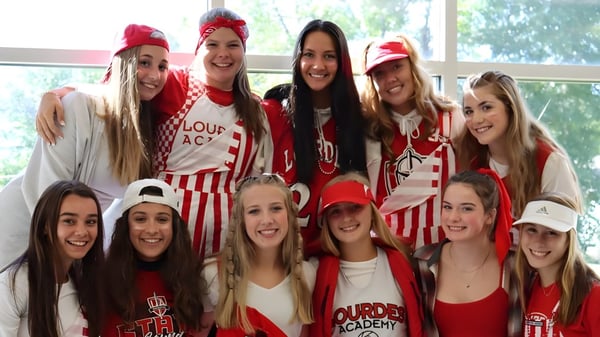 Un grupo de jóvenes estudiantes posan con ropa roja y blanca en el campus de Lourdes Academy.
