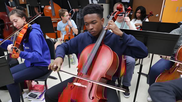 Un alumno de la Lowell Catholic High School toca intensamente un gran violonchelo rojo durante un ensayo de música.