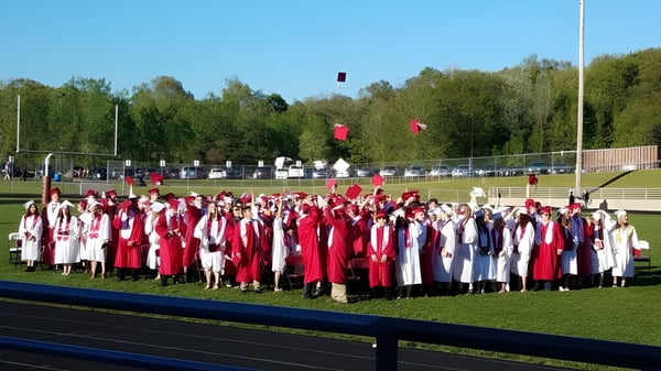 Estudiantes de la Lowell High School se reúnen en togas rojas y blancas en el campo deportivo para su ceremonia de graduación.