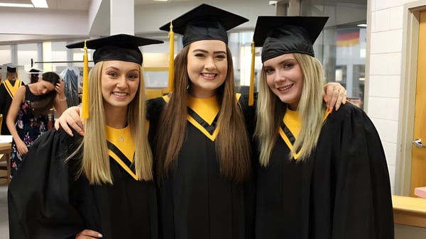 Tres estudiantes en togas de graduación posan juntas en el campus de Luther College High School.