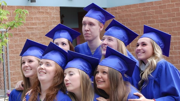 Un grupo de graduadas y graduados sonrientes de la L.V. Rogers Secondary School está frente a un edificio de ladrillo.