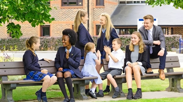 Un grupo de alumnas y alumnos está sentado en un banco frente a un edificio de ladrillo en el campus de LVS Ascot.