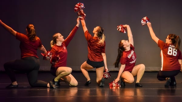 Estudiantes del Lyndon Institute bailan con trajes rojos en un escenario con iluminación tenue.