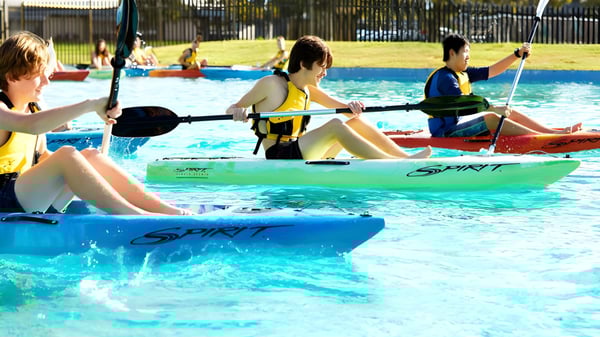 Estudiantes de la Lynwood Senior High School en actividades de deportes acuáticos con kayaks coloridos en una piscina exterior.