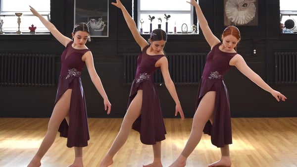 Tres estudiantes en vestidos burdeos de la Macdonald High School realizan una rutina de baile en un estudio.